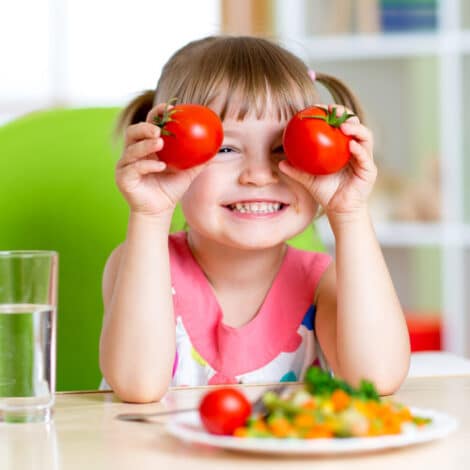 Child with tomatoes. Happy girl with vegetables at home.