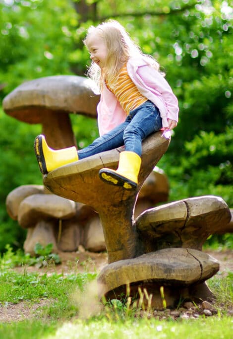 Two cute little sisters having fun on giant wooden mushrooms
